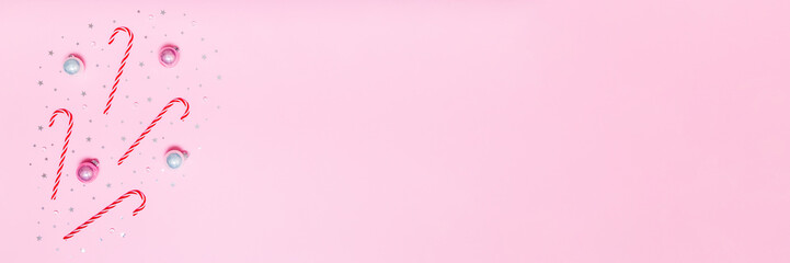 Pink holiday background with candy canes, baubles and silver stars arranged on left side, leaving wide copy space for festive banners, promos or seasonal designs