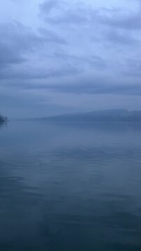 Mist and fog over lake and pond. Murky, gloomy and dark nature in the evening, sundown, and nightfall. Melancholic, calm, peaceful and gloomy landscape. Vertical panning video.