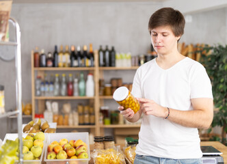 Obraz premium Young male shopper chooses olive in jar in grocery store