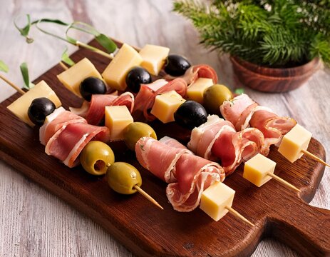 pinchos de jamon queso y aceitunas verdes y negras presentados en tabla rustica con decoracion natural