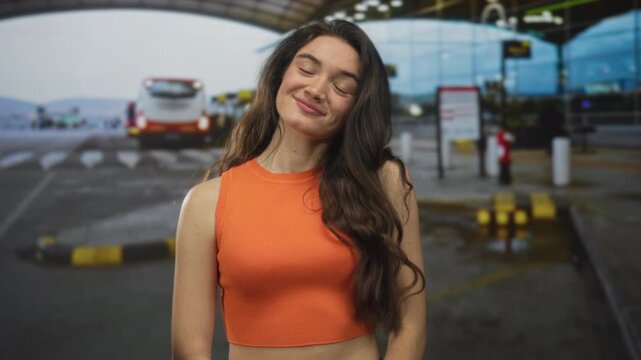 Woman with bare midriff making callme gesture with hand at airport terminal dropoff area; connection communication playfulness.