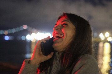 Joyful young woman laughing on smartphone at night