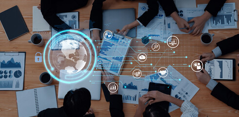 A diverse team of business professionals engages in data analysis and strategy discussion, surrounded by digital icons that symbolize global connectivity and technology. Trope