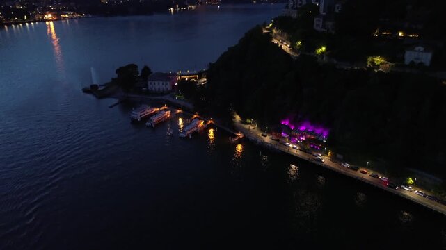 cinematic nocturnal aerial drone view of dazzling lights over Lake Como with motorboats leaving white trails on the blue waters 4