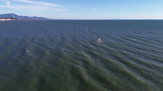 Cinematic aerial view of windsurfers performing acrobatics on a windy winter day along the blue Italian coast 2