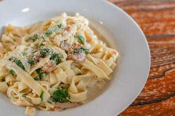 Close-up shot of creamy fettuccine pasta with spinach, mushrooms, and grated parmesan served in a white plate on a rustic table. Ideal for culinary projects, restaurant menus, and Italian food content