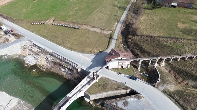 Aerial drone footage of a serene river winding through the lush springtime plains of Piedmont near Cuneo province with warm sunlight illuminating the rural Italian countryside and rolling green meadow