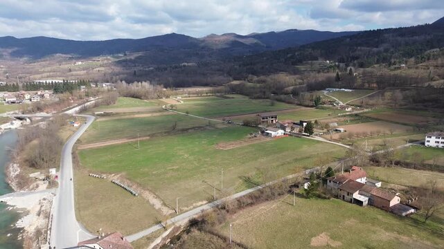 Aerial drone footage of a serene river winding through the lush springtime plains of Piedmont near Cuneo province with warm sunlight illuminating the rural Italian countryside and rolling green meadow