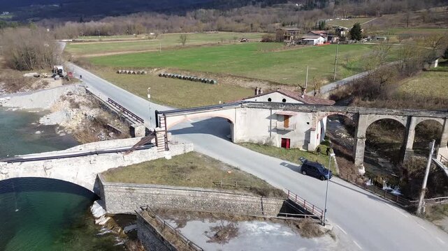 Aerial drone footage of a serene river winding through the lush springtime plains of Piedmont near Cuneo province with warm sunlight illuminating the rural Italian countryside and rolling green meadow