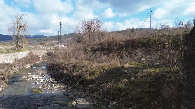 Aerial drone footage of a serene river winding through the lush springtime plains of Piedmont near Cuneo province with warm sunlight illuminating the rural Italian countryside and rolling green meadow