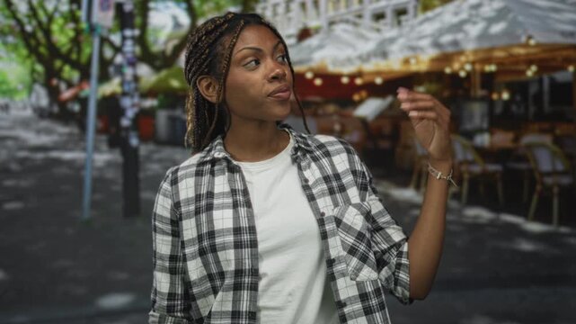 Woman with braided hair wearing white tee and plaid shirt points index finger up on restaurant terrace under string lights; confidence reminder.