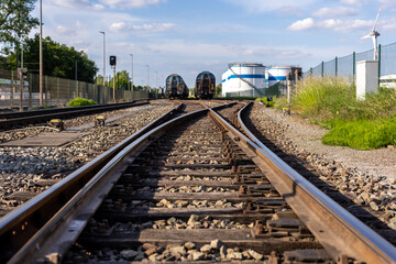 Naklejka premium Rusty railway switch toward parked tank wagons under bright blue sky background sunny day. Industrial yard shows metal tracks gravel storage tanks oil refinery plant factory station