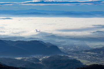 A panoramic view from the high plateau shows surrounding mountain ranges and a valley densely covered in a thick layer of inversion fog