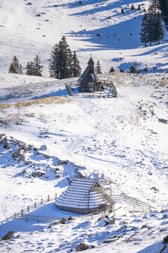 Wooden Shepherd&rsquo;s Chapel (Kapela Marije Snežne) and a traditional hut stand amidst a snow-covered high mountain pasture in the Kamnik-Savinja Alps