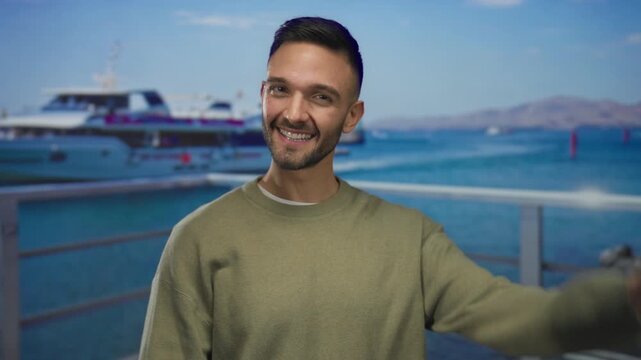 Young man making ok gesture with both hands and smiling on a seaside promenade with boats in the background on a sunny day