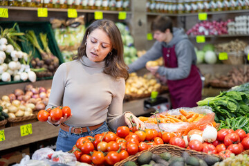 Delighted young woman customer taking tomatoes from vegetable box in big greengrocery