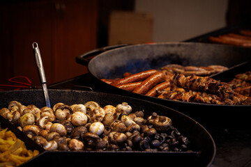 Grilled mushrooms sausages and meat skewers cooking at street food market stall