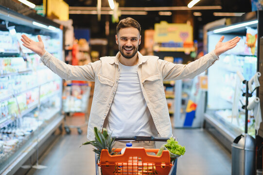 Man smiling shopping in supermarket with full cart - Powered by Adobe
