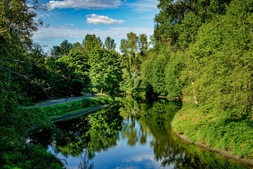 Obraz premium People walk on a riverside path in a sunny park near Kenmore Washington