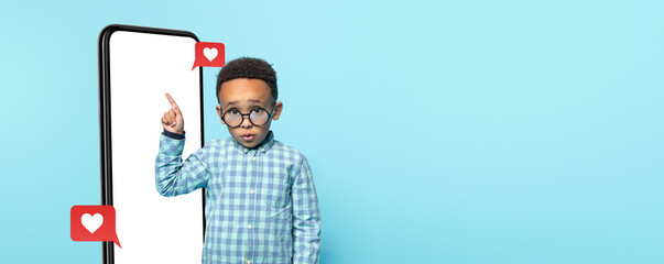 A young child with glasses stands in front of a large smartphone with heart symbols around them.