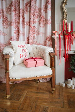 A wrapped gift and a festive Christmas cushion on an armchair next to a fireplace decorated with ribbons tied around candlesticks