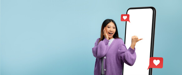 A young woman stands beside a tall, blank screen, smiling with excitement. She makes a hand gesture to invite viewers to engage with her joyful expression in a colorful setting.