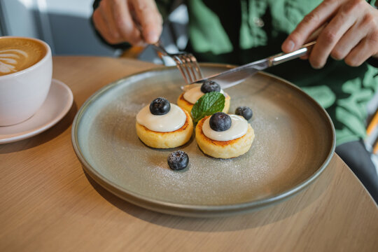 Close-up of a man sitting at a table eating Mini Pancakes with fresh yogurt, Blueberries, mint and a cappuccino