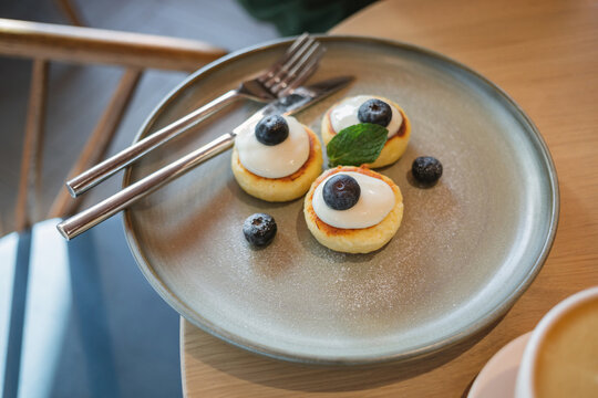 Close-up of a plate of Mini Pancakes with fresh yogurt, Blueberries, mint and a cappuccino on a table