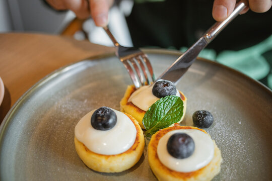 Close-up of a man sitting at a table eating Mini Pancakes with fresh yogurt, Blueberries and mint