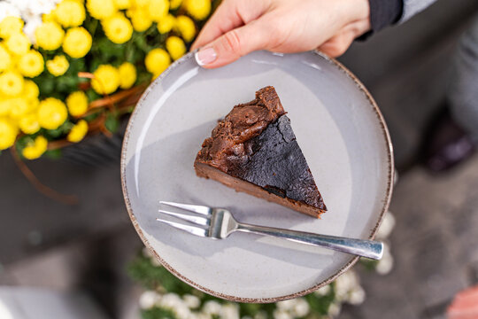 Overhead view of a woman standing outdoors holding a plate with a slice of chocolate Burnt Basque cheesecake