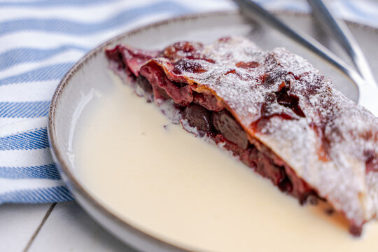 Close-up of a slice of cherry strudel with hot vanilla sauce on a garden table