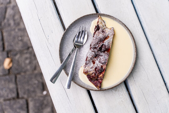 Overhead view of a slice of cherry strudel with hot vanilla sauce on a garden table