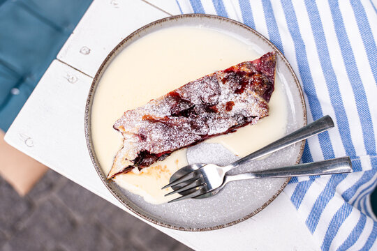 Overhead view of a slice of cherry strudel with hot vanilla sauce on a garden table