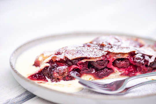 Close-up of a slice of cherry strudel with hot vanilla sauce on a garden table