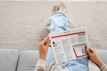Naklejka premium Young woman with newspaper sitting on sofa at home, top view