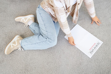 Young woman with blank newspaper on carpet at home, top view