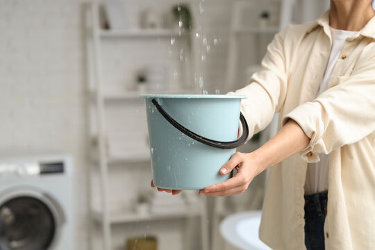 Young woman placing bucket under water dripping from ceiling in bathroom, closeup
