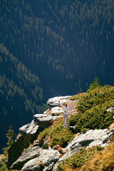 Young woman on cliff edge above deep forest valley in Fagaras Mountains, Romania. Transfagarasan Highway. Freedom, solo travel, mindfulness concept.