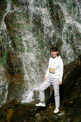 Young smiling woman traveler standing on rocks at Capra Waterfall in Fagaras Mountains. Transfagarasan Highway, Romania.