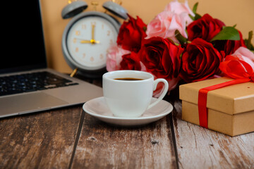 cup of coffee with gifts and roses on a wooden table