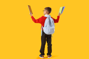 Little schoolboy with tablet computer and books on yellow background