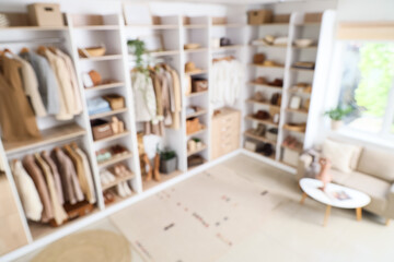 Blurred view of wardrobe with stylish clothes, organizers and sofa
