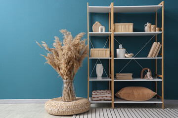 Bookshelf with stylish decor and pampas grass near blue wall in room