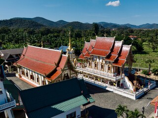 Ornate Thai temple buildings with red roofs against mountain backdrop