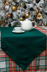 Teapot and cup on green table runner over plaid Christmas table