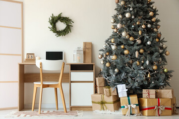 Interior of festive home office with workspace, Christmas tree and gift boxes