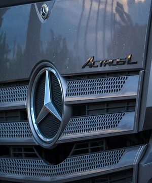 Front view detail of gray Mercedes Benz Actros L truck grill with large chrome star logo and model lettering on the metal mesh