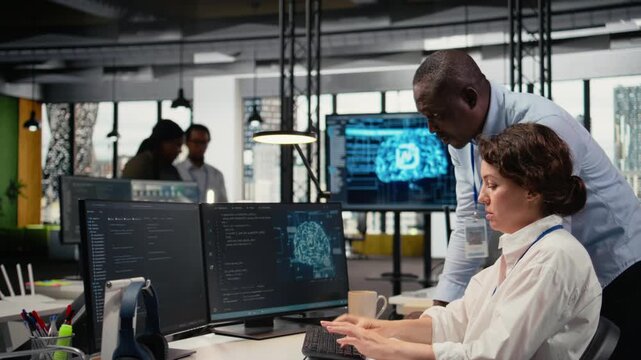 Manager supervises intern in startup office using artificial intelligence driving market innovation. Tech agency team leader shows trainee how to to optimize operations with machine learning, camera A