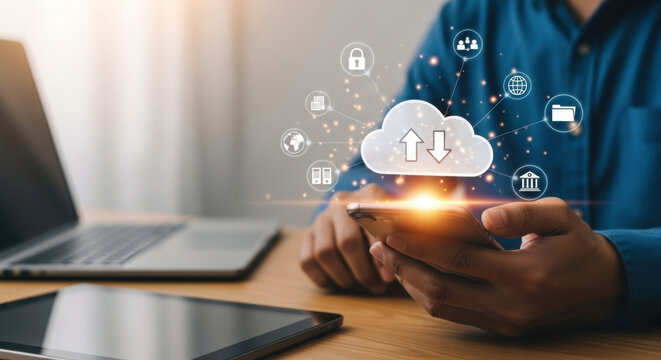 A man in a blue shirt uses a smartphone near a laptop and tablet on a wood table, highlighted by a cloud computing icon. - Powered by Adobe