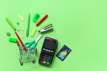 Payment terminal, credit card and shopping cart with different stationery on green background
